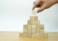 A hand is placing a piece of wood into a pyramid