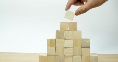 A hand is placing a piece of wood into a pyramid